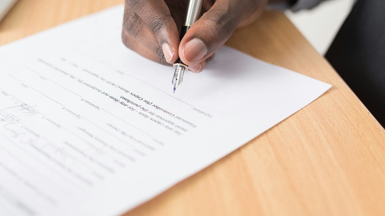 A hand signing a printed document on a desk