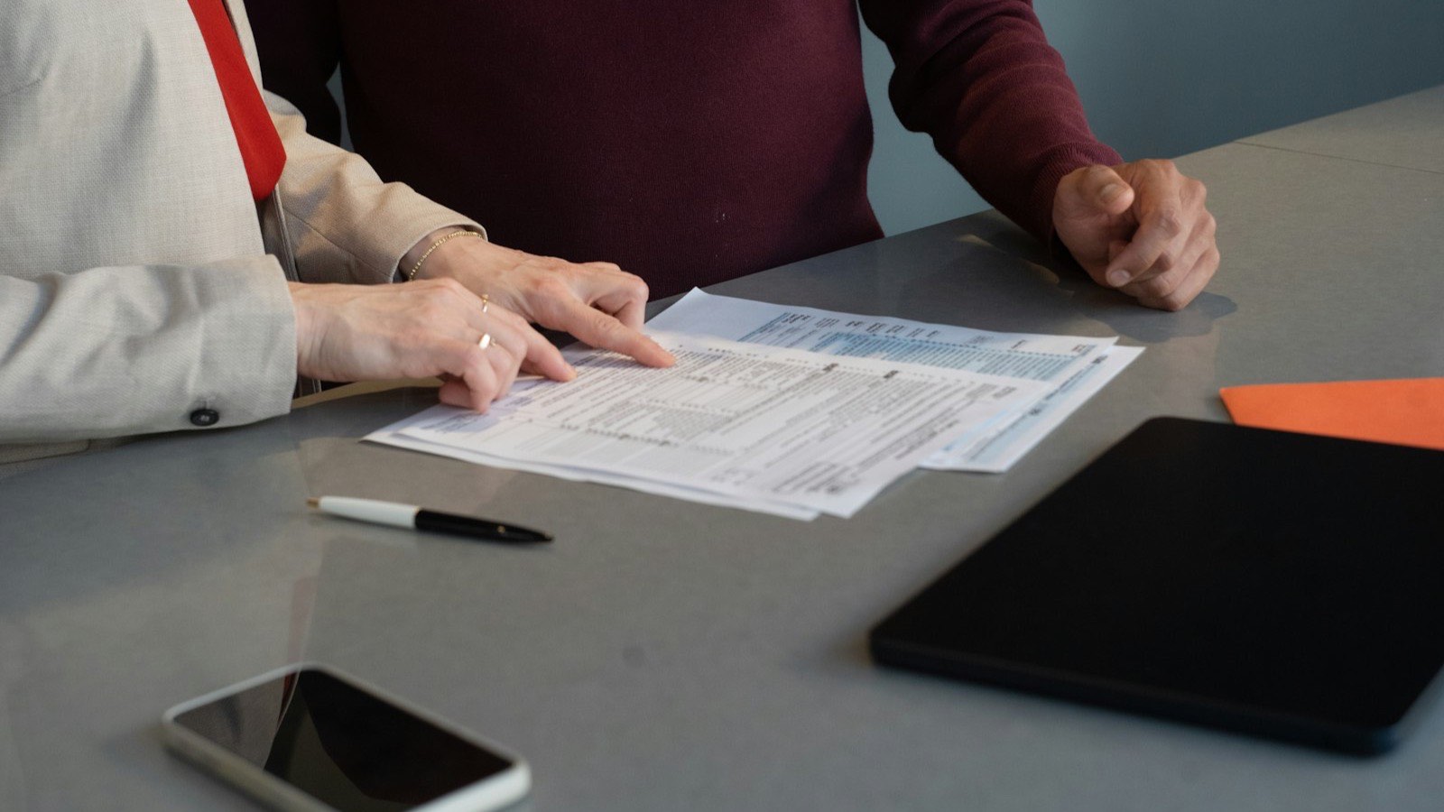 Two people discuss forms printed at a table