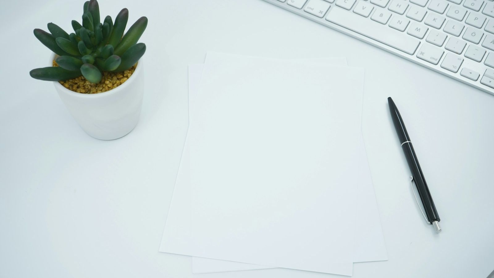Empty sheets paper with ballpoint pen and keyboard on a bright desk