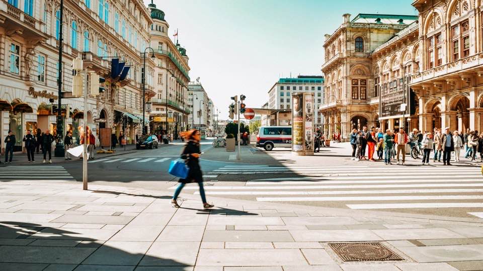 Passanten überqueren die Kreuzung an der Wiener Staatsoper bei Tageslicht